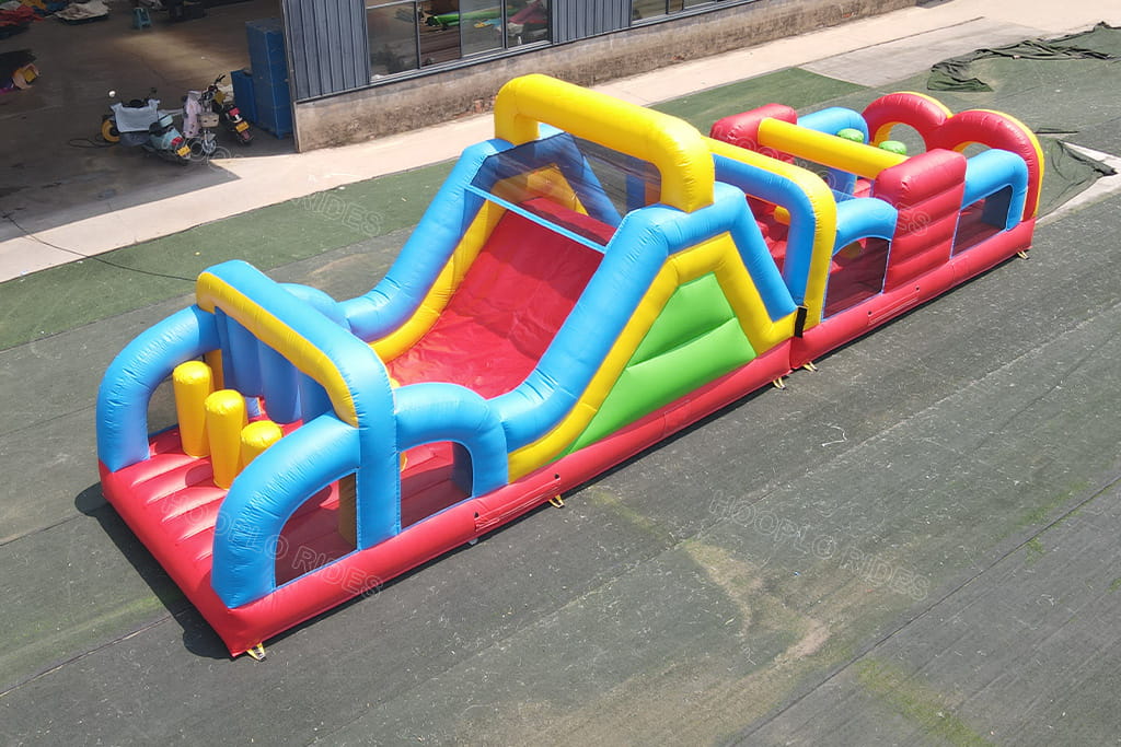 Hooplo Rainbow Inflatable Obstacle Course Top Front Aerial View, Commercial Kids Outdoor Challenge Game With Slide, Crawl Tunnels & Soft Bump Pillars