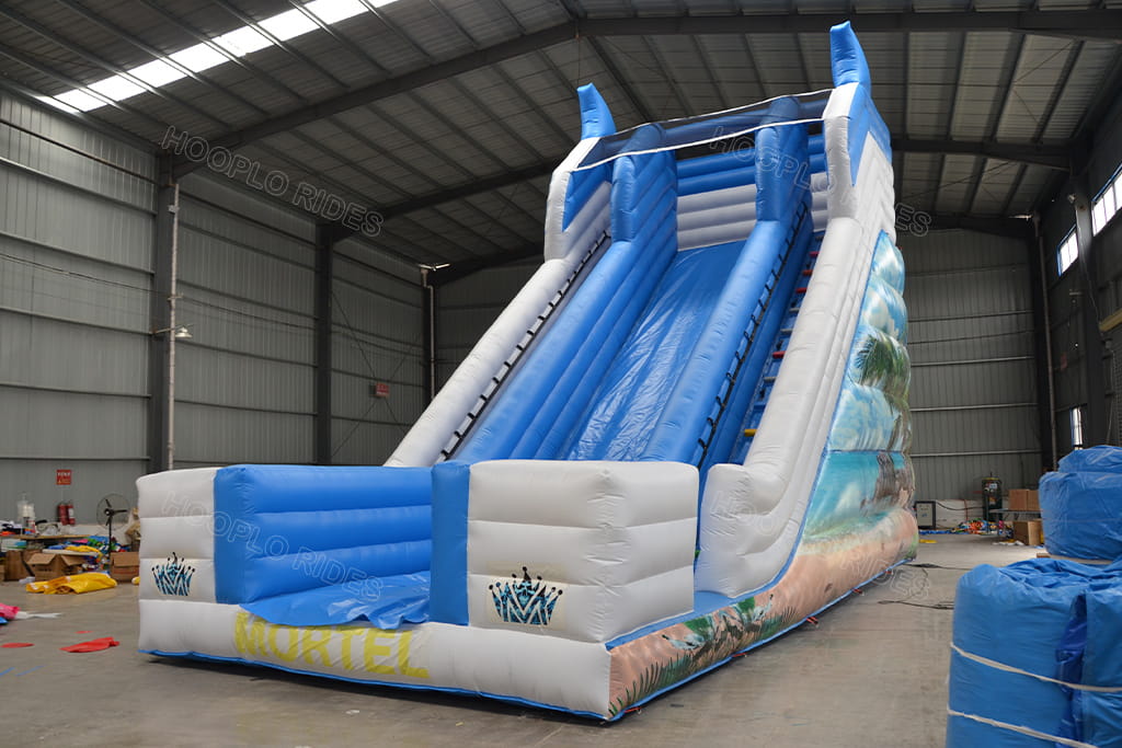 Workshop shot of big beach themed inflatable dry slide for party rental business, white‑blue color scheme