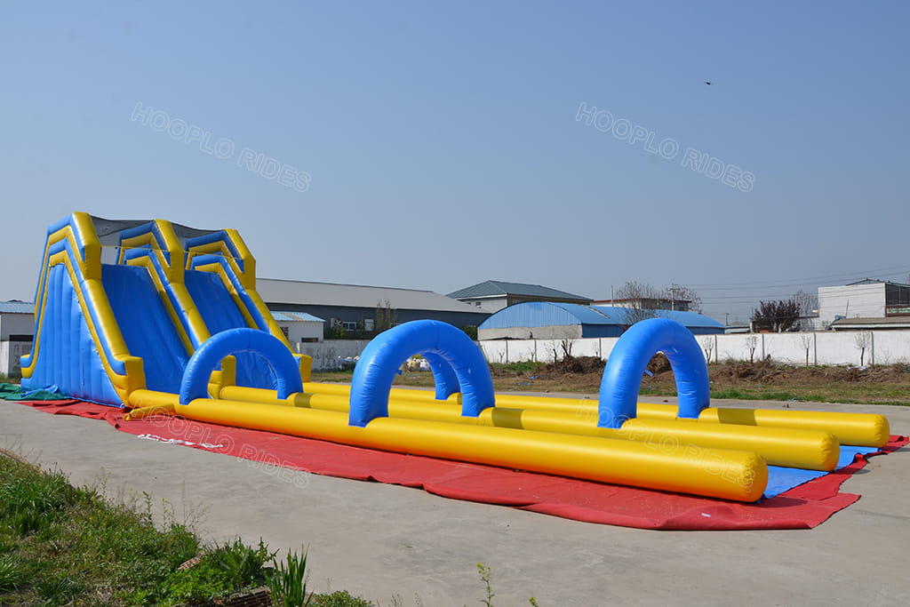 Ground front full view of commercial dual‑lane inflatable water slide with sequential blue arch obstacles, outdoor giant inflatable racing slide for carnival and water park