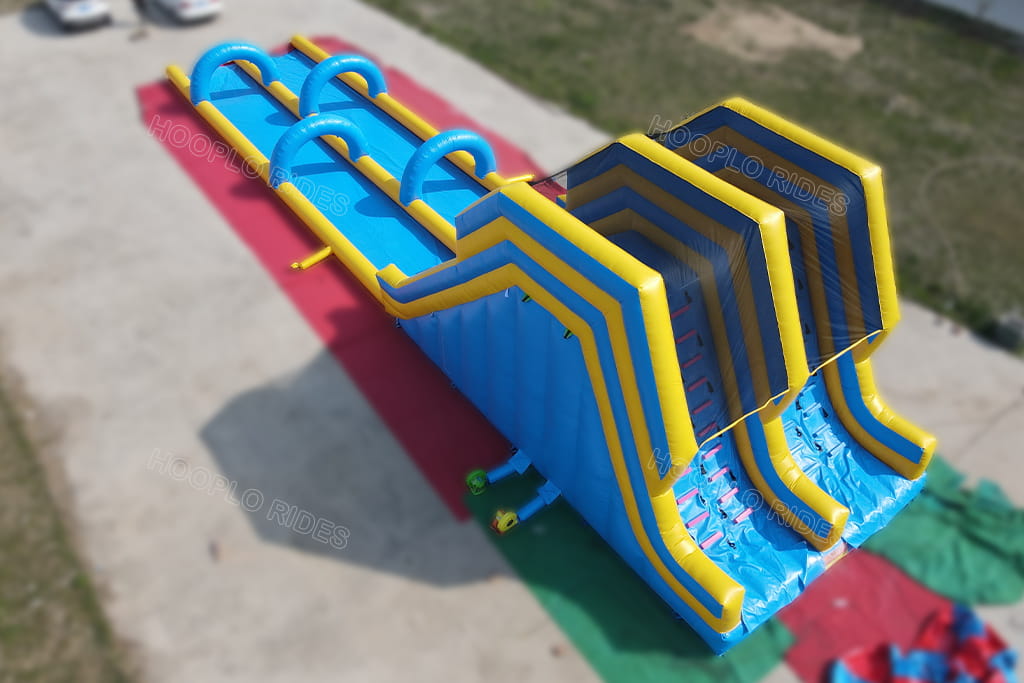 High‑angle shot of large dual lane inflatable water slide, showing rear climbing ladder and slide top safety net for commercial rental business