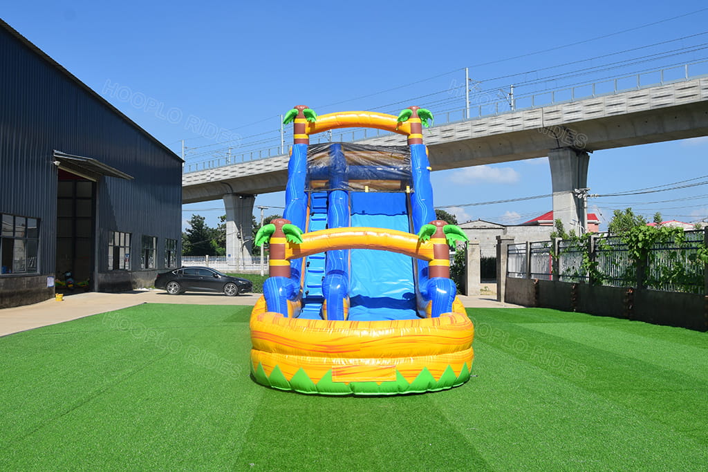 Front view tropical inflatable water slide decorated with palm trees, inflatable slide with landing pool for summer events
